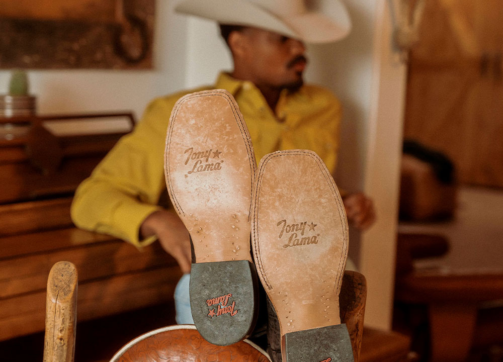 A Cowboy Leaning Against a Piano Bench Wearing the Sealy 13" Western Boots in Brown